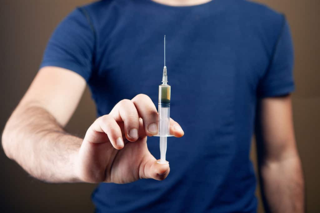 man holding a filled syringe. addiction concept on brown background